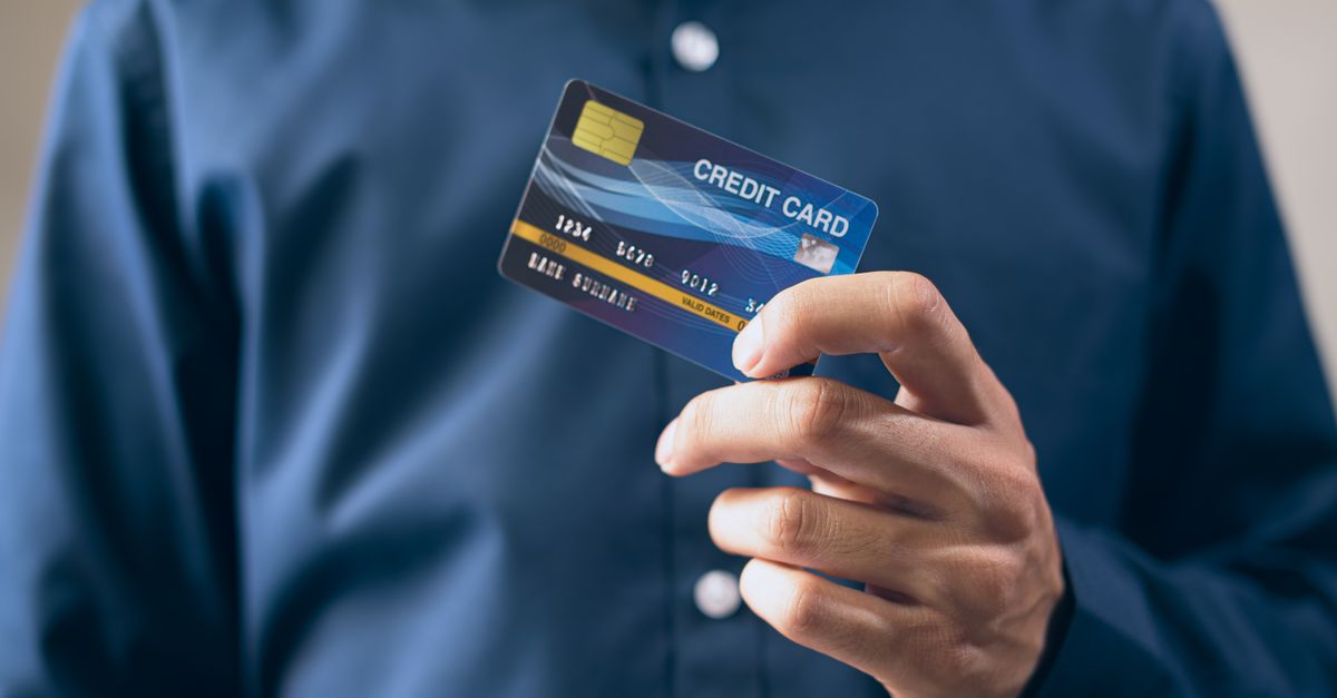 Close-up of a person holding a credit card in a hand, wearing a button-up shirt.